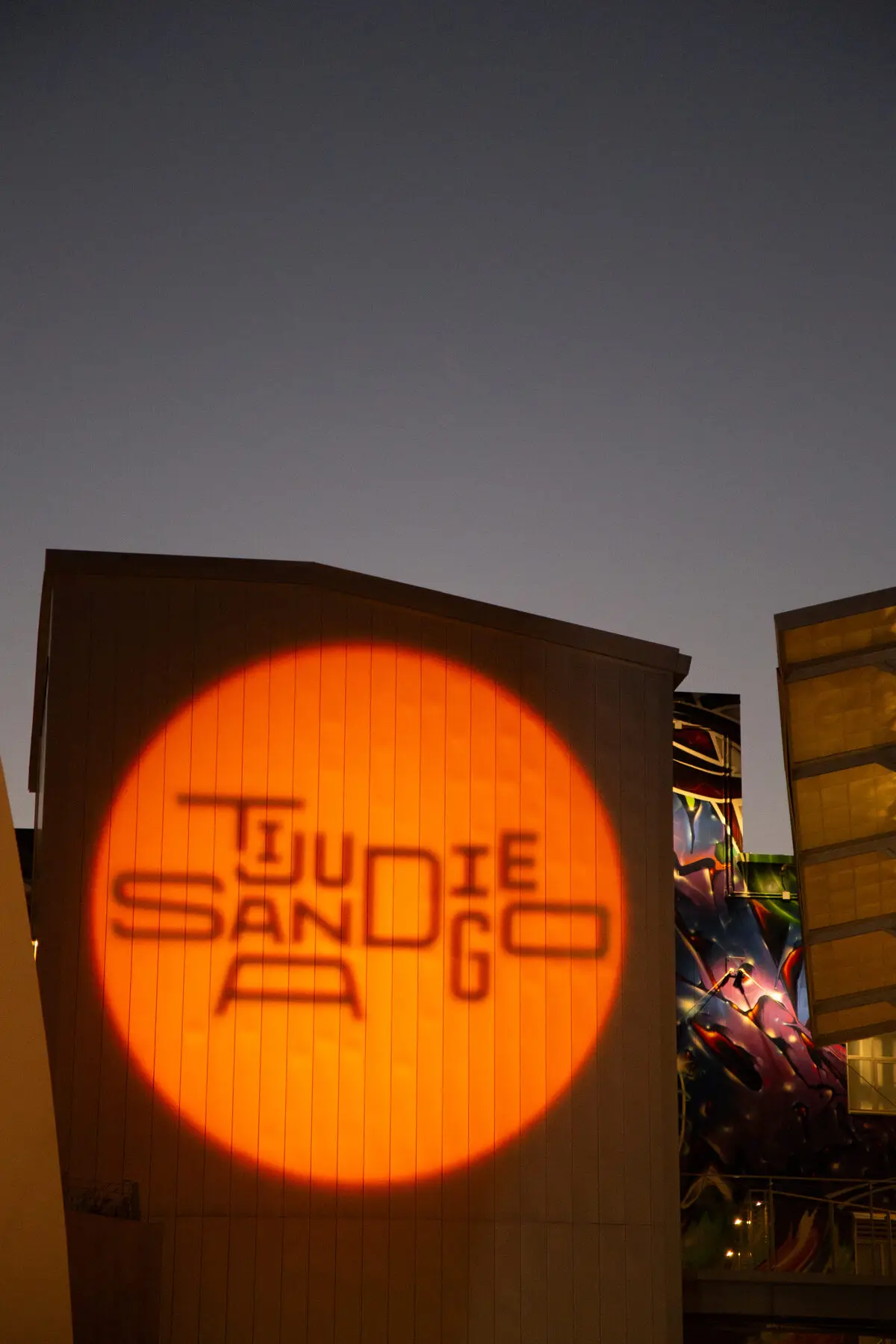 An orange Tijuana San Diego logo projected on a building at dusk
