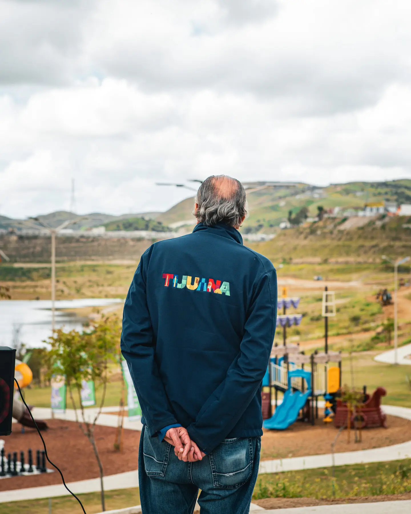 A man in a jacket embroidered with Tijuana looks out over a new park