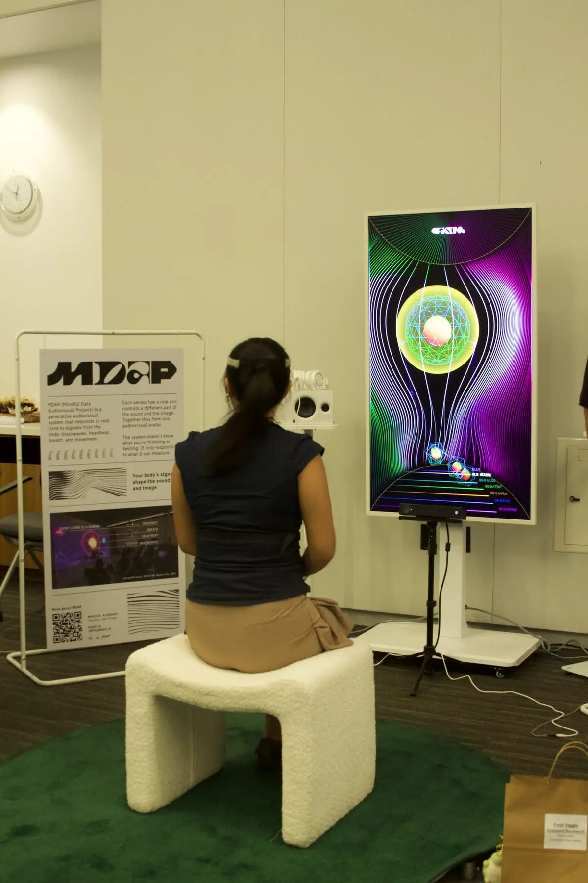 An attendee wearing an EEG headband sits before a vertical screen showing a glowing generative avatar